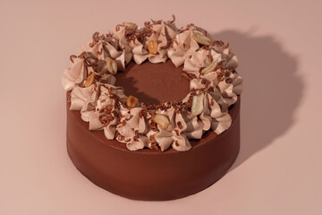 Round bento cake with chocolate frosting and decorative whipped cream topping, featuring nuts and chocolate shavings, beautifully presented on a soft pink background, ideal for celebrations