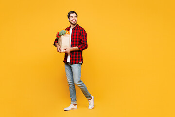 Full body young happy man wear casual clothes hold paper bag for takeaway mock up with food products walk go look aside isolated on plain yellow orange background. Delivery service from shop concept.