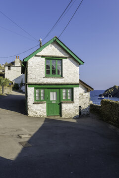 Looe, United Kingdom - 04 October 2025: View of a quaint white cottage with vibrant green trim, nestled near the coast where the sea meets the rugged cliffs.