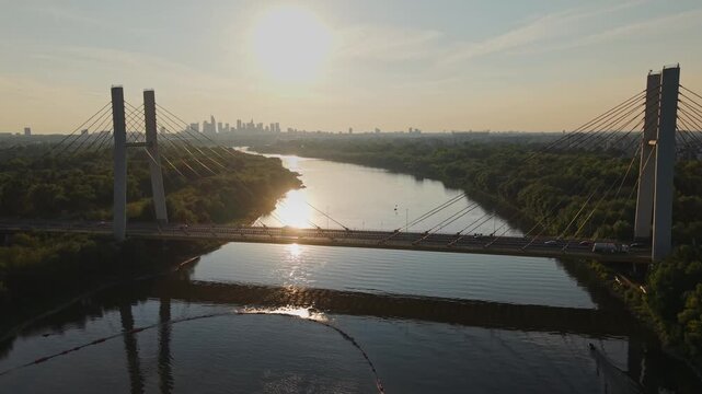 Aerial view of Siekierkowski (Siekierki) bridge over Vistula river, on which cars move on a sunny day. Warsaw, Poland. Modern skyscrapers and Warsaw business center on the horizon.