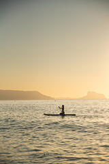 Fototapeta premium Young woman paddleboarding in serene ocean at sunset