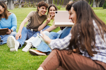 Happy students doing selfie with digital tablet sitting on grass at college campus park - Back to school, university lifestyle and diversity gender concept concept - Main focus on center people faces