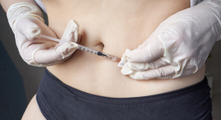 Hispanic female administering insulin injection in abdomen with gloves on for diabetes management.