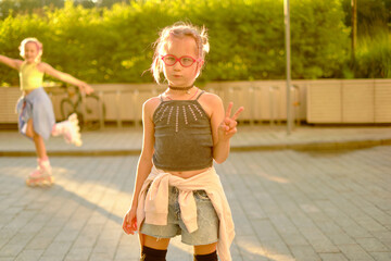 Young girl with pink glasses skateboarding outdoors at sunset, wearing casual black top and tied-around denim shorts with pink skates, embodying childhood joy and energetic outdoor fun