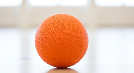 Fototapeta premium Vibrant Orange Ball Resting on Polished Wooden Floor of an Indoor Sports Court or Gymnasium, Ready for Play and Activity