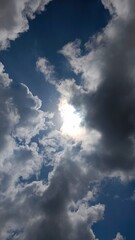 Bright sun hiding behind dramatic dark and white clouds in a blue sky

