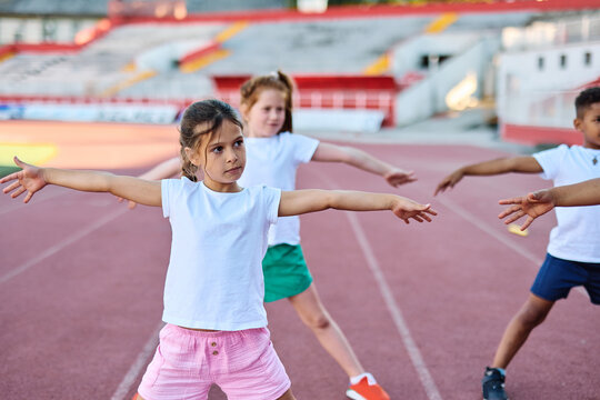 Children exercising and stretching at the stadium, practice during sports class in school training, little boys and girls in sportswear training as athletes outdoor. Concept of sport, fitness and ach - Powered by Adobe