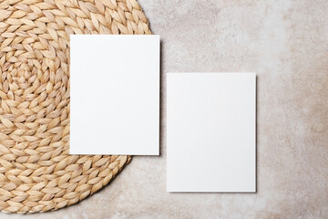 Two blank white invitation or greeting cards mockup on a round woven placemat, showcasing a minimalist design with natural textures and neutral tones for creative design purposes