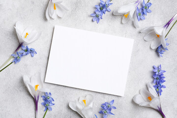 Blank greeting or invitation card surrounded by delicate white and blue flowers on a textured gray background, creating a serene and inviting atmosphere for design and creativity