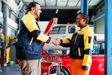 Two diverse auto technicians shake hands in a professional garage setting, showing teamwork, trust, and successful collaboration in a modern, inclusive automotive service environment.