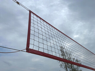 Upward Close-Up of an Outdoor Volleyball Net Against a Cloudy Sky and Tree Background