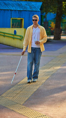 Blind man with cane walking on tactile paving in colorful accessible park. Concept of urban...