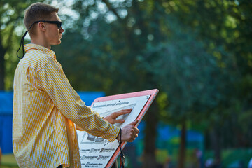 Blind man reading tactile map with hands in outdoor park environment. Concept of assistive tech, education, accessibility, inclusive exploration and public info.
