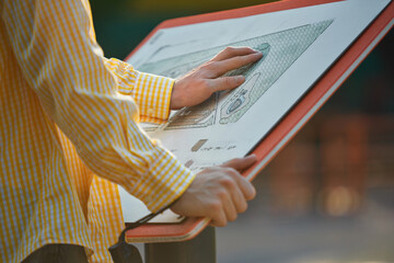 Tactile map used by blind man in yellow shirt at outdoor information stand. Concept of urban accessibility, assistive tech, social inclusion, and educational tools.