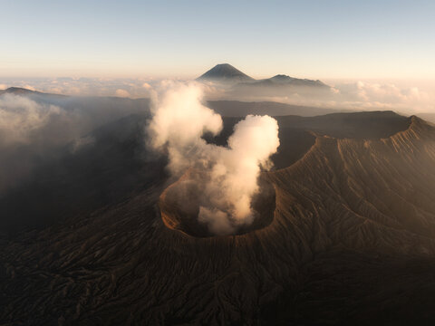 Aerial view of the majestic Mount Bromo volcano smoking with the crater's dark depths contrasting against the ethereal wisps of clouds, Bromo Tengger Semeru National Park, East Java, Indonesia.