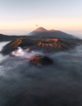 Aerial view of the majestic Mount Bromo shrouded in ethereal mist, its volcanic peaks piercing the dawn, creating a dramatic landscape, Bromo Tengger Semeru National Park, East Java, Indonesia.