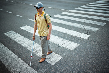 Fototapeta premium Blind man walking independently with cane on pedestrian crossing. Concept of assistive tech, social inclusion, mobility training, and awareness.