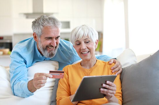 portrait of happy smiling senior elderly couple using a tablet computer and a credit card for online shopping at home, technology and internet use in everyday life concept