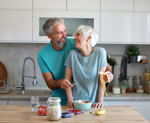 Portrait of a senior mature couple bonding, hugging and having a healthy breakfast after fitness exercise training in the morning at home