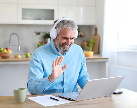Portrait of a senior mature man or businessman having a video call on laptop wearing headphones  in his home office at home - Powered by Adobe