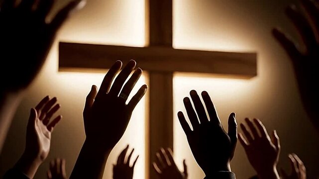 Silhouetted hands reach upwards towards a glowing wooden cross on a soft lit wall
