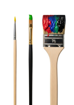 Three artist's paintbrushes with wooden handles and metal ferrules, featuring dabs of vibrant yellow, green, red, blue, and black paint, standing upright against a transparent studio background with