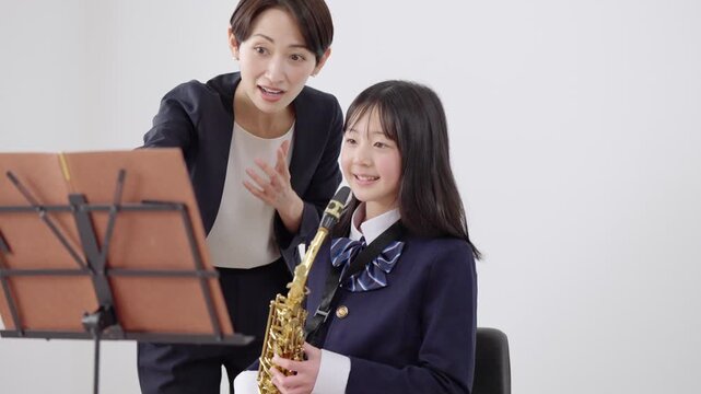 サックスを吹くブラスバンド部員と顧問の女性教師
