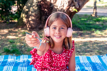 Smiling girl sharing food at park picnic while wearing headphones