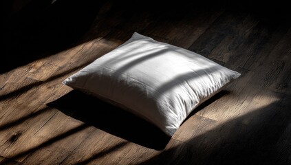 A pristine white pillow rests on a dark wood floor, bathed in sunlit stripes.  The image is minimalist and evokes a sense of calm