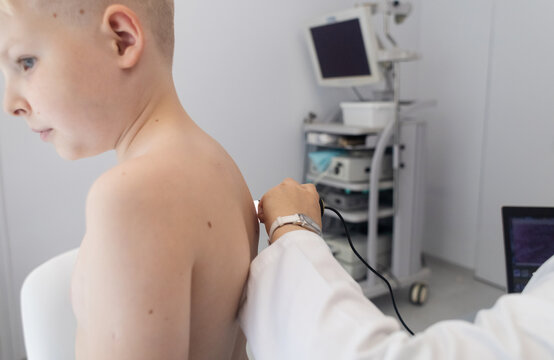 A pediatric dermatologist examining a young boys skin with a dermatoscope in a medical clinic. Skin check up for moles and birthmarks. - Powered by Adobe