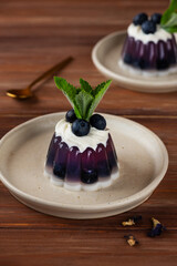Jelly with blueberries, mint, anchan tea and cream with agar agar on a brown wooden table. Summer dessert, gelatin free. Vertical orientation.