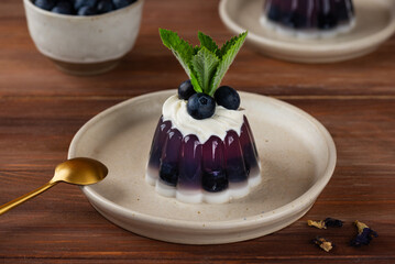 Violet jelly with fresh blueberries, mint, anchan tea and cream with agar agar on a wooden table. Summer dessert, gelatin free.