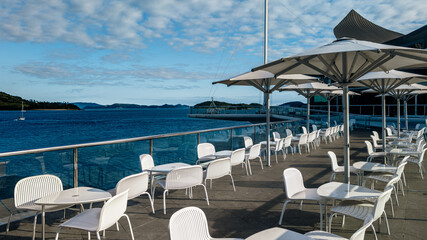  Outdoor seating alongside a sea with distant green hills and a clear blue sky.