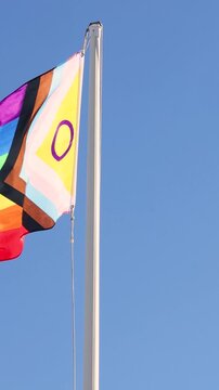 Intersex-inclusive redesign of the Progress Pride Flag. Rainbow LGBT flag against a blue sky. Flag fluttering in the wind. An abbreviation that stands for lesbian, gay, bisexual, transgender