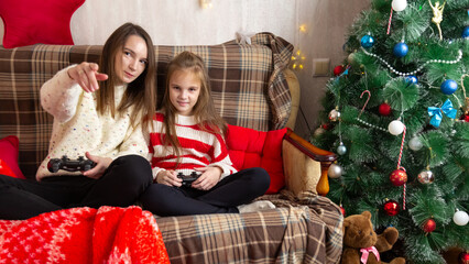 Happy family mother and daughter laugh and play video games together using a video game console on christmas holiday
