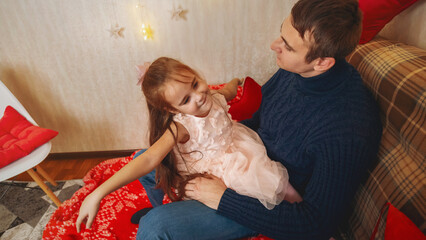 Smiling father and daughter sitting on the sofa at home near the Christmas tree