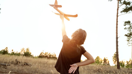 Girl play with toy airplane. Children toy plane in hands of child in summer in park under sun. Concept of child's dream of flying, child runs across field at sunset.