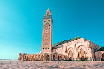 Hassan II Mosque with its minaret towering over the paved square under the vibrant blue sky in...