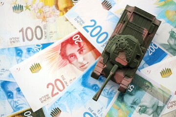 Israel New Shekels banknotes and toy tank. The current Israel money bills and tank lies on table