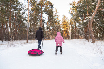 Father and daughter having fun with snow tube in the forest