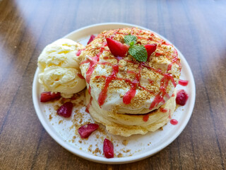 plate of fluffy Japanese souffle pancakes topped with whipped cream, crushed graham crackers, strawberry sauce, fresh strawberry slices, and a scoop of vanilla ice cream on the side.