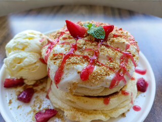 plate of fluffy Japanese souffle pancakes topped with whipped cream, crushed graham crackers, strawberry sauce, fresh strawberry slices, and a scoop of vanilla ice cream on the side.