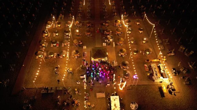 Aerial View of Event: An elevated perspective captures a nighttime event, with scattered lights illuminating tables and a central gathering, exuding a festive atmosphere. Rimini, Italy