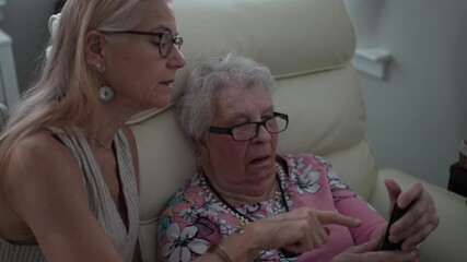 A daughter assists her elderly mother in making a phone call at a senior living facility, focusing on dialing and enhancing her memory skills.