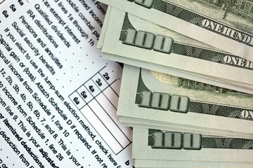 Big amount of United States hundred dollar bills on table with tax return form close up