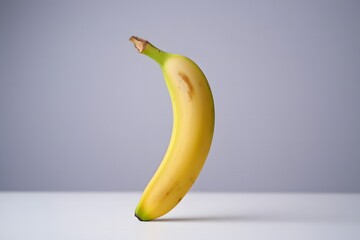 A single ripe yellow banana standing upright on a white surface against a light purple background