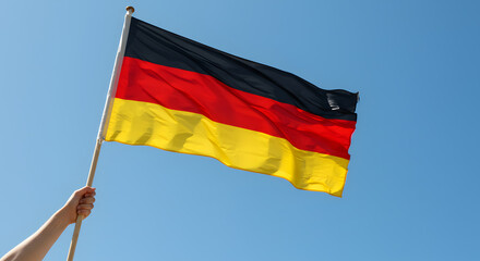 German National Flag Waving in Blue Sky, Held by Hand &ndash; Symbol of Patriotism and Identity