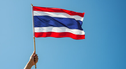 Patriotic Hand Holding Thailand Flag Against Bright Blue Sky