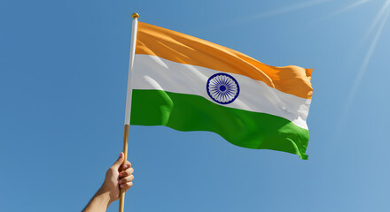 Hand proudly holding the Indian national flag waving in a bright blue sky with sunlight