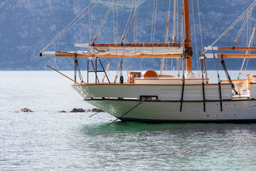 Front and center, a moored sailboat rests in calm waters, its wooden mast and taut rigging framed against a misty mountain backdrop